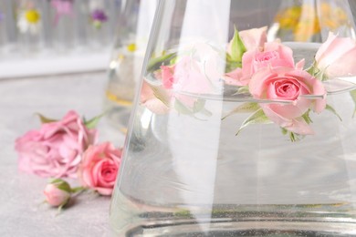 Flask with rose flowers on table, closeup. Essential oil extraction