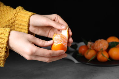 Woman peeling fresh ripe tangerine on black background, closeup