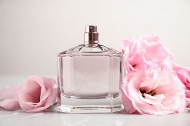 Bottle of perfume with fresh flowers on light background
