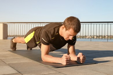 Sporty man doing plank exercise on mat outdoors