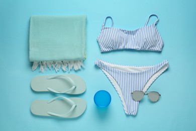 Beach towel, swimsuit, flip flops and sunglasses on light blue background, flat lay