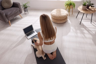 Woman with dog watching online yoga class at home, back view