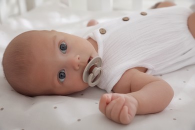 Cute little baby with pacifier lying on bed, closeup
