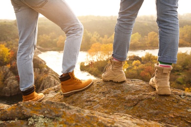 Couple wearing stylish hiking boots on steep cliff, closeup