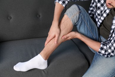 Man rubbing sore leg on sofa, closeup