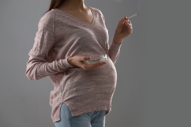 Young pregnant woman smoking cigarette on grey background. Space for text