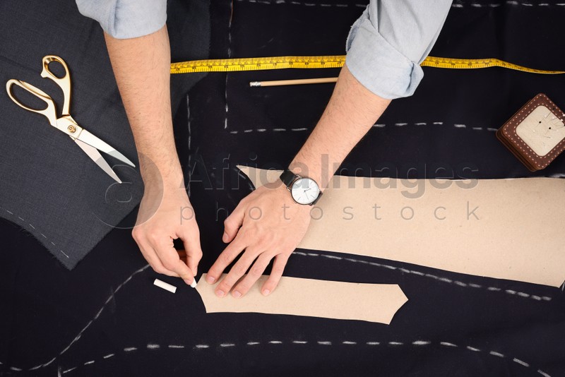 Photo of Tailor marking sewing pattern on fabric with chalk at table, top view