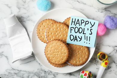 Cookies with toothpaste and HAPPY FOOL'S DAY note on white marble table, flat lay. April holiday