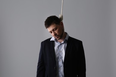Depressed businessman with rope noose on neck against light grey background