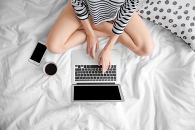 Female blogger with laptop and cup of coffee on bed, top view