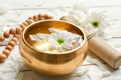 Golden singing bowl with flower, mallet and beads on white wooden table, closeup. Sound healing
