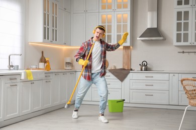 Handsome young man with headphones singing while cleaning kitchen