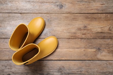 Yellow rubber boots on wooden background, top view. Space for text