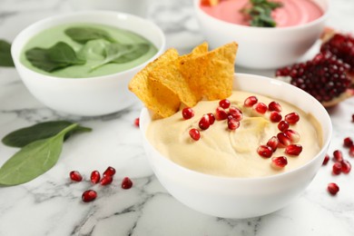 Bowl of delicious classic hummus with tortilla chips and pomegranate seeds on white marble table