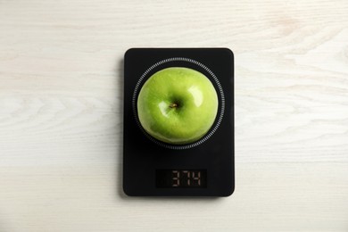 Ripe green apple and electronic scales on white wooden table, top view