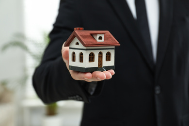 Real estate agent holding house model indoors, closeup