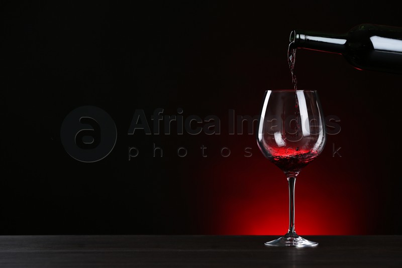 Pouring wine from bottle into glass on table against dark background, space for text