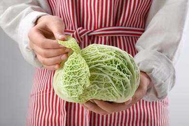Woman separating leaf from fresh savoy cabbage on light grey background, closeup