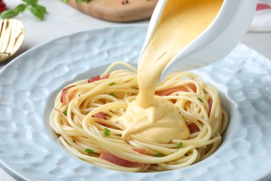 Pouring tasty cheese sauce onto spaghetti with meat, closeup