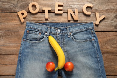 Photo of Men jeans with banana and nectarines symbolizing male genitals near word Potency on wooden table, flat lay