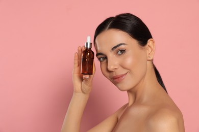 Young woman with bottle of essential oil on pink background. Space for text