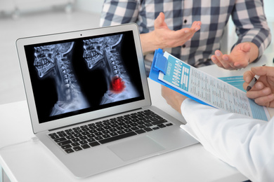 Image of Doctor consulting man in clinic, closeup view. Focus on laptop displaying x-ray of patient with cancer