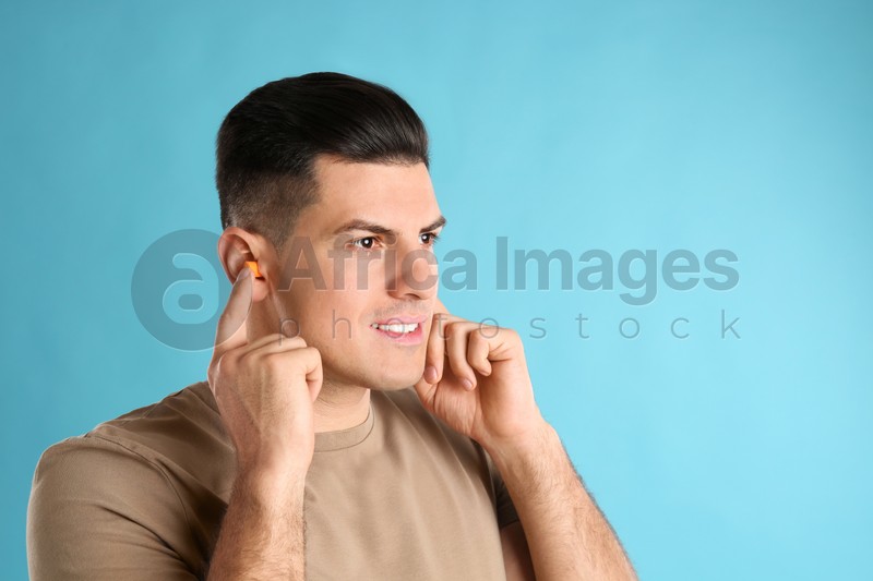 Man inserting foam ear plugs on light blue background. Space for text