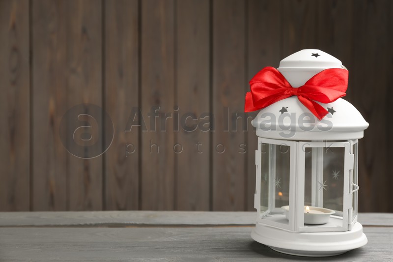 Photo of Beautiful decorative Christmas lantern with burning candle on grey wooden table. Space for text