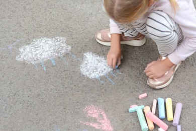 Photo of Little child drawing white clouds with chalk on asphalt, closeup