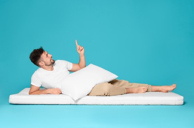Man with pillow on soft mattress pointing upwards against light blue background