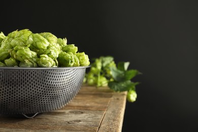 Photo of Fresh green hops on wooden table against black background, space for text