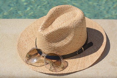 Stylish hat and sunglasses near outdoor swimming pool on sunny day. Beach accessories