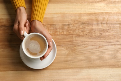 Woman holding cup of coffee at wooden table, top view. Space for text