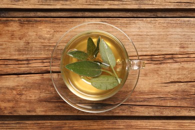 Cup of aromatic sage tea with fresh leaves on wooden table, top view