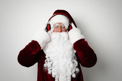 Santa Claus with headphones listening to Christmas music on light background
