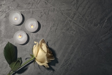 Beautiful white rose and candles on grey background, top view. Funeral symbol