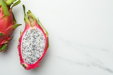 Photo of Delicious cut and whole dragon fruits (pitahaya) on white marble table, flat lay. Space for text