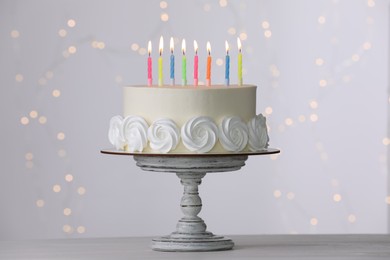 Birthday cake with burning candles on white table against blurred festive lights