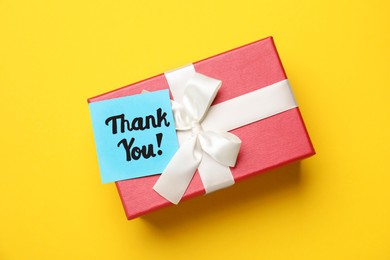 Gift box and light blue paper note with phrase Thank You on yellow background, top view