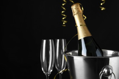Happy New Year! Bottle of sparkling wine in bucket and glasses on black background, space for text