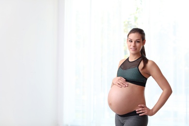 Young pregnant woman in fitness clothes at home. Space for text