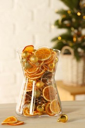 Photo of Glass vase with dry orange slices, cones and Christmas tree balls on white wooden table. Festive decor