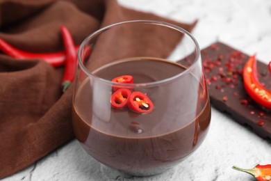 Photo of Glass of hot chocolate with chili pepper on white textured table, closeup
