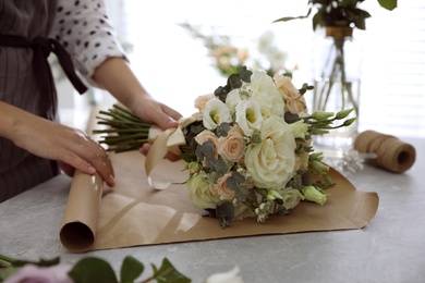 Florist making beautiful wedding bouquet at light grey marble table, closeup
