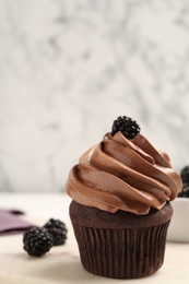 Delicious chocolate cupcake with cream and blackberries on white board, closeup. Space for text