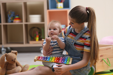 Photo of Teen nanny and cute little baby playing with xylophone at home