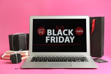 Laptop with Black Friday announcement, notebooks and gifts on pink background