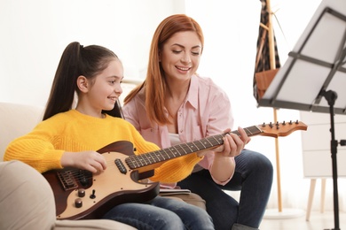 Little girl playing guitar with her teacher at music lesson. Learning notes