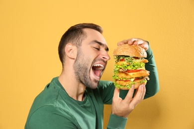 Photo of Young hungry man eating huge burger on color background