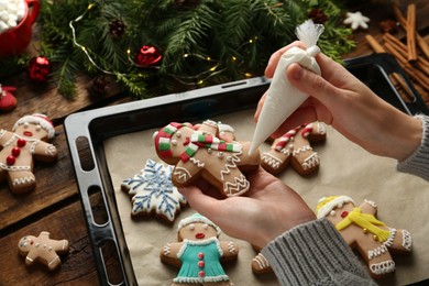 Making homemade Christmas cookies. Girl decorating gingerbread man at wooden table, closeup